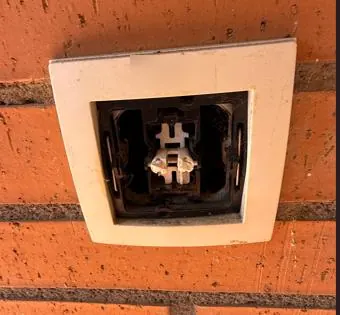 Caja de timbre en una pared de ladrillo, sin pulsador y con el mecanismo a la vista