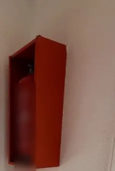 Extintor dentro de un armario metálico rojo en una pared, sin señal que lo indique